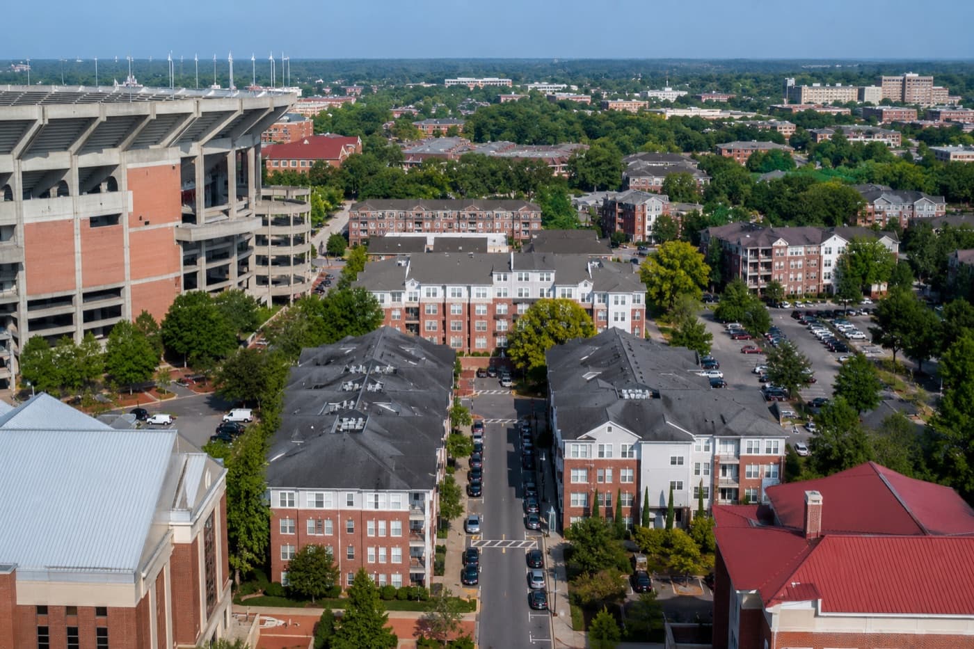 Aerial view of brick apartment buildings lining a street beside a college football stadium.